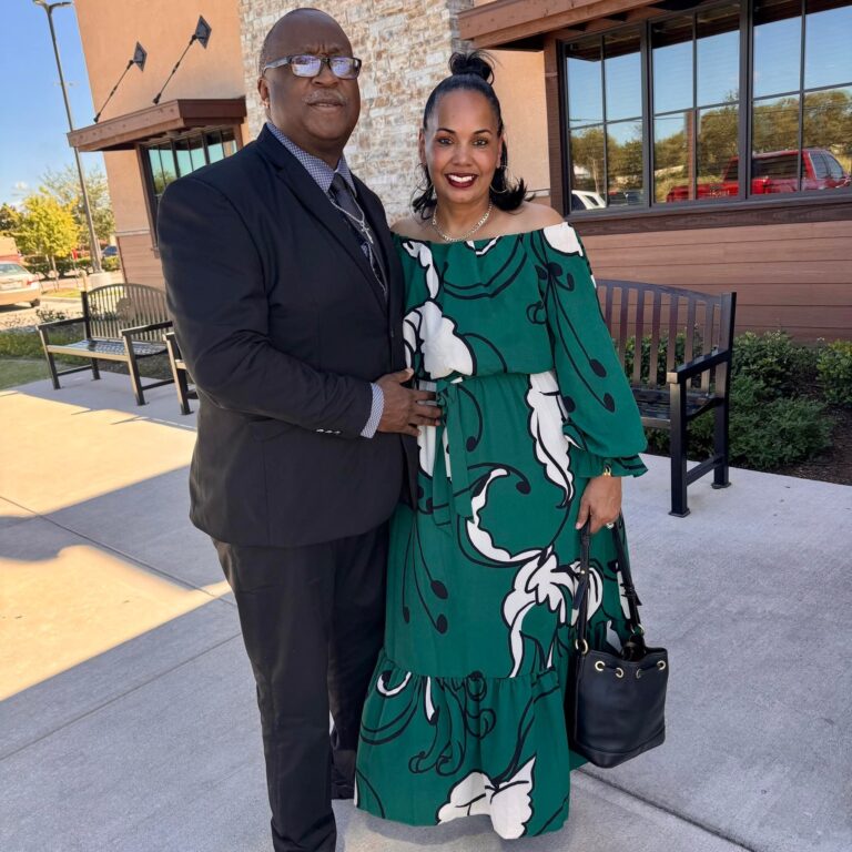Black man with glasses wearing a black suit. Black woman with medium dark brown/black hair in half up (bun top) half down hairstyle wearing a long sleeve green white and black dress