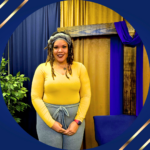 Black lady with medium brown to black locs wearing a long sleeve yellow blouse and grey pants